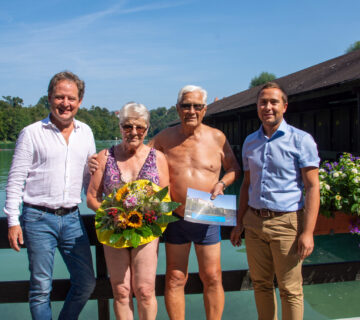 Erster Bürgermeister Florian Schneider und Bäderleiter Stefan Sajdak überreichen dem Ehepaar Hausperger Blumen und Saisonkarten für das nächste Jahr am Wöhrsee. Fotocredit: Stadt Burghausen