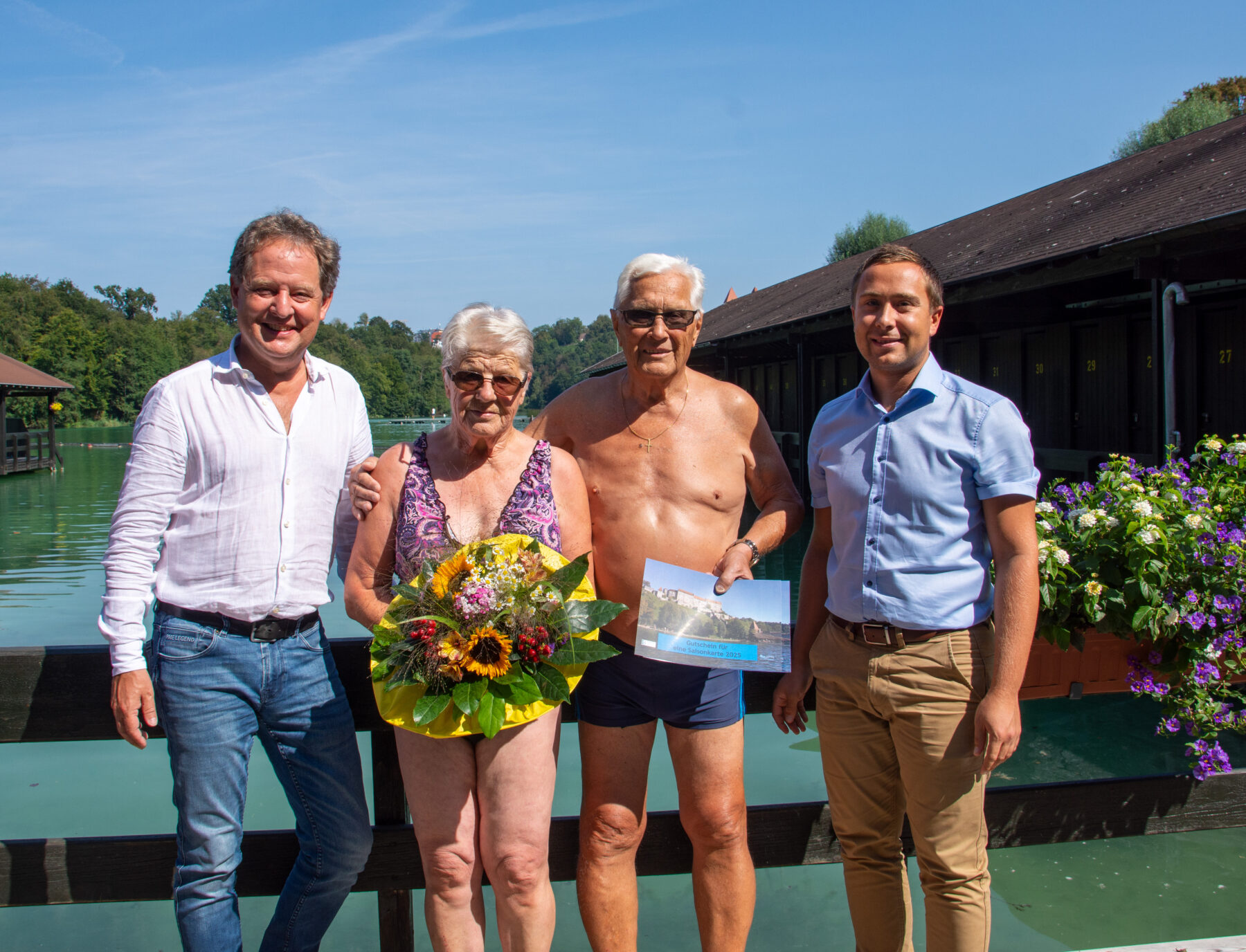 Erster Bürgermeister Florian Schneider und Bäderleiter Stefan Sajdak überreichen dem Ehepaar Hausperger Blumen und Saisonkarten für das nächste Jahr am Wöhrsee. Fotocredit: Stadt Burghausen