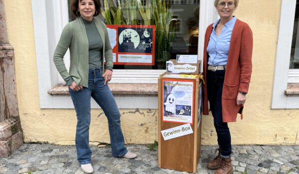 In der Stadtbibliothek ist das Gespenst Toni derzeit nicht zu übersehen. Christin Moll (li.), Leiterin der Stadtbibliothek, und Mitarbeiterin Rosi Pfeifenthaler am Startpunkt des Bilderbuch-Spaziergangs Fotocredit: Stadt Burghausen/sast