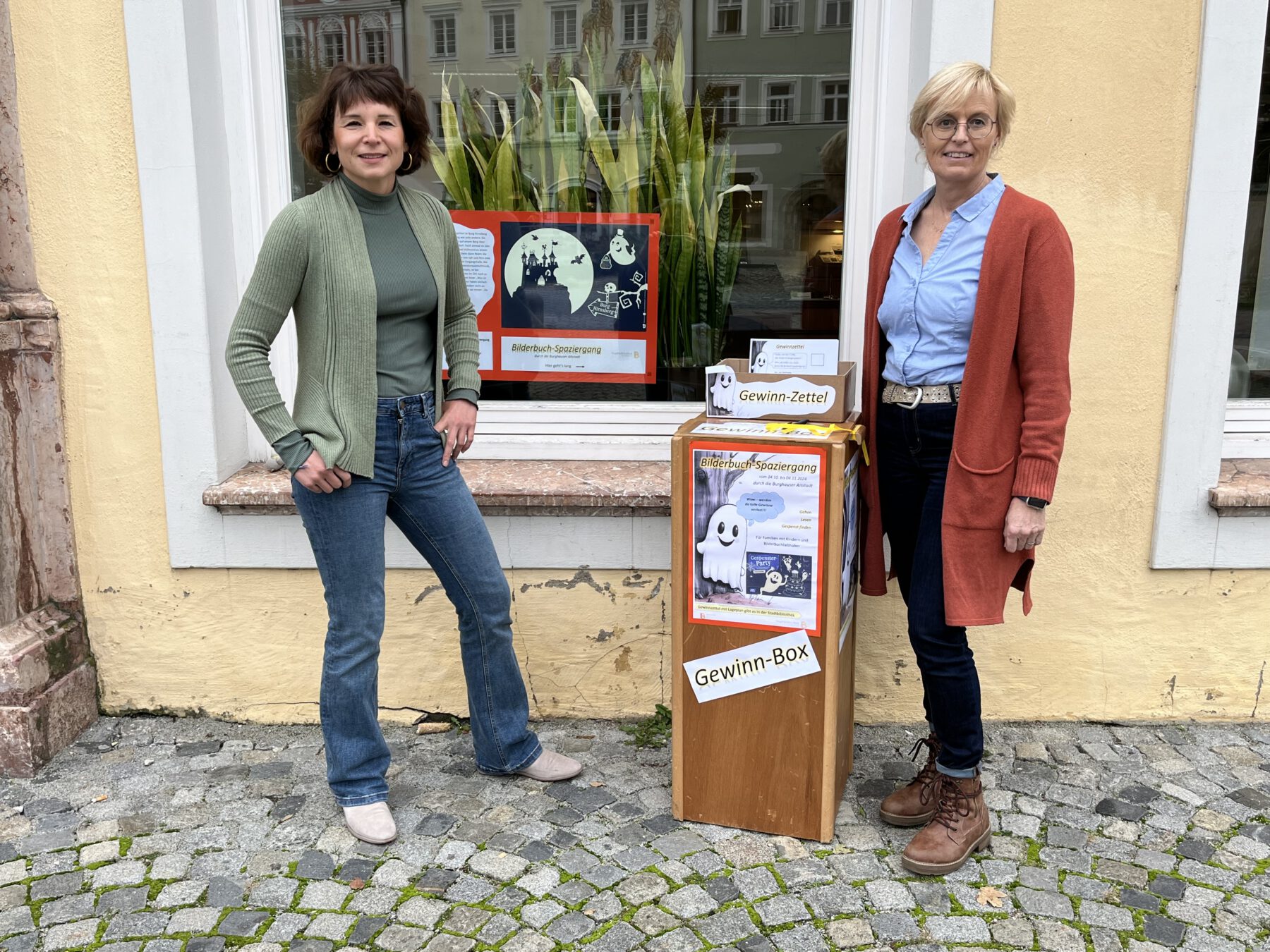 In der Stadtbibliothek ist das Gespenst Toni derzeit nicht zu übersehen. Christin Moll (li.), Leiterin der Stadtbibliothek, und Mitarbeiterin Rosi Pfeifenthaler am Startpunkt des Bilderbuch-Spaziergangs Fotocredit: Stadt Burghausen/sast